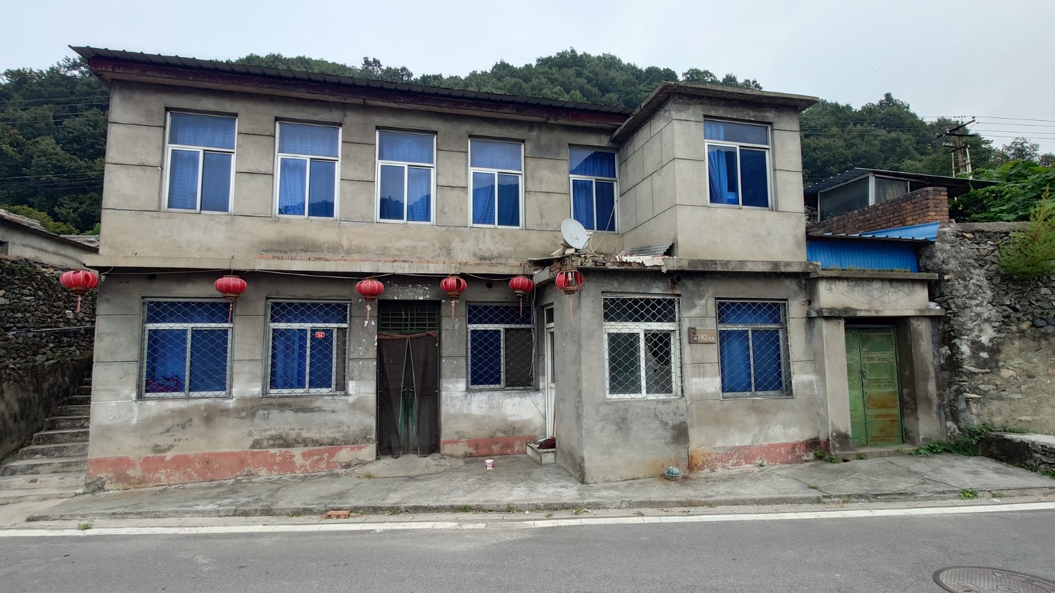 A boxy two-storey cement village house with blue window coverings
