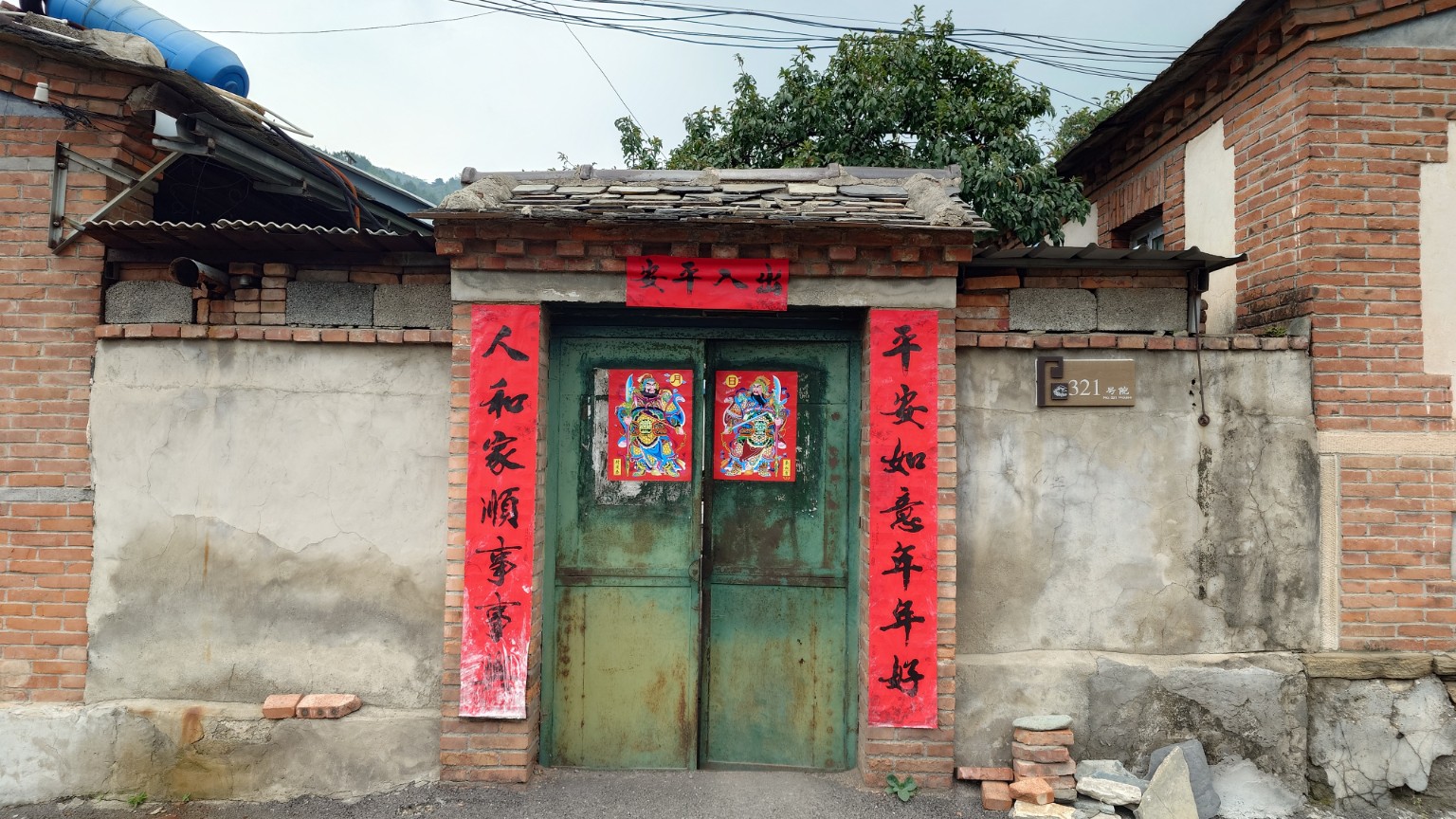 A numbered Nanjiao courtyard with an old green metal gate and red couplets