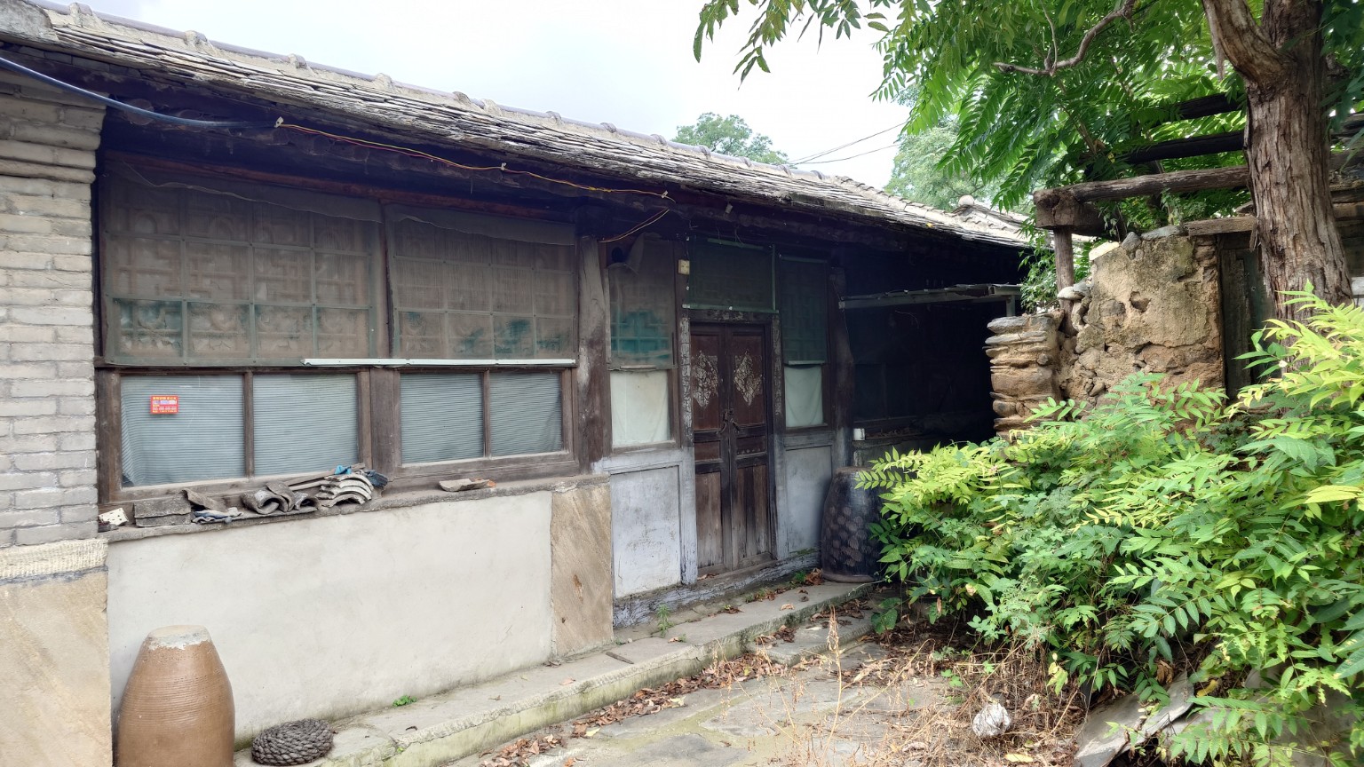 A weathered timber-fronted courtyard house partly reclaimed by vegetation