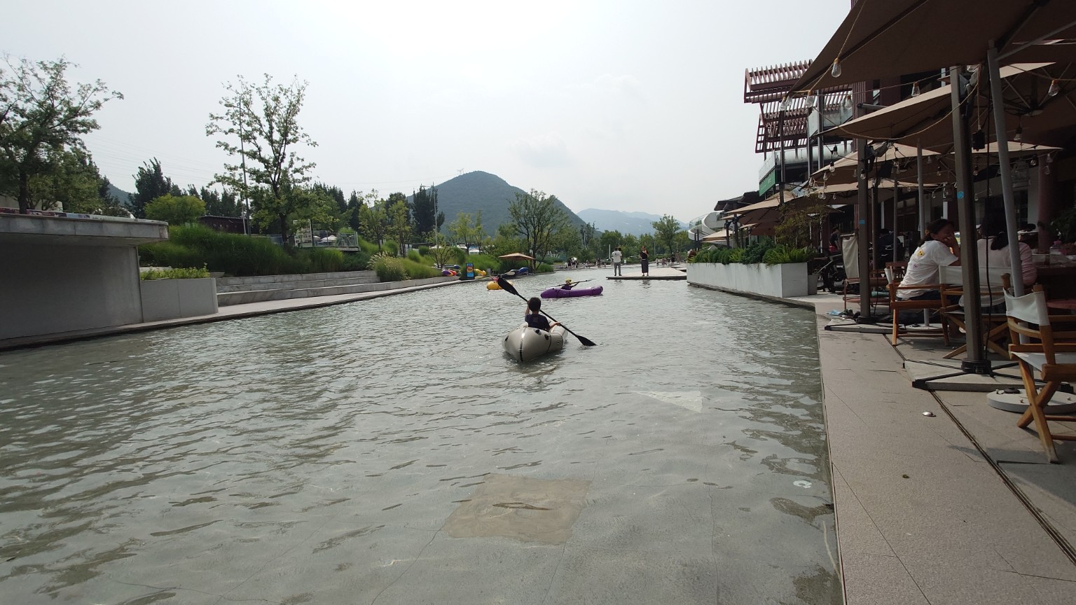 Children paddling in a shallow Tanzhesi canal beside outdoor restaurant terraces