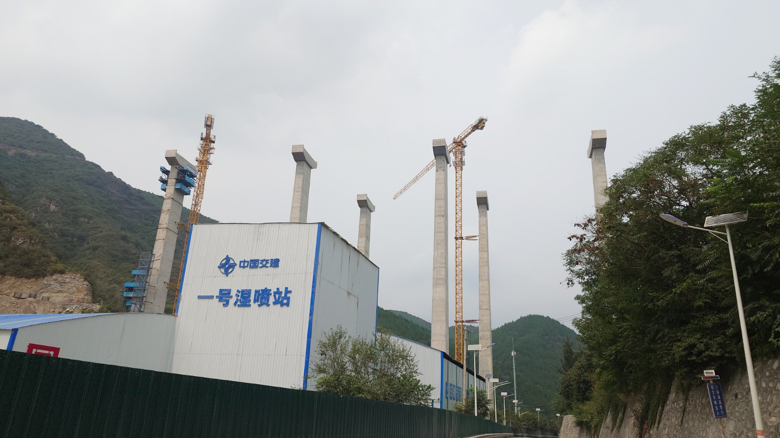 Tall concrete bridge piers and tower cranes rising from a western Beijing mountain valley