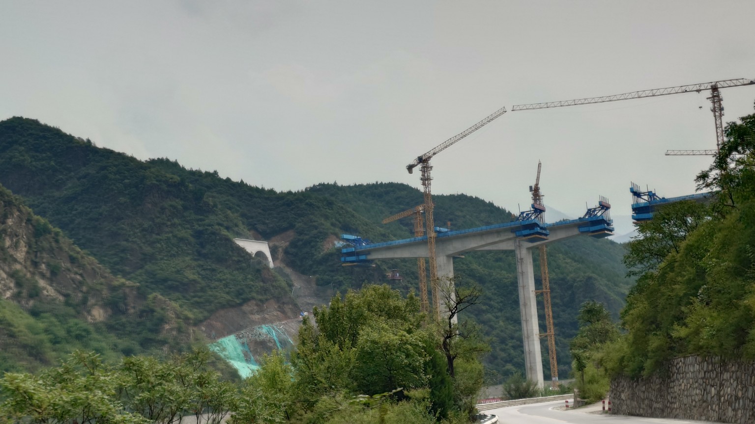 An expressway viaduct under construction beside a tunnel portal in a western Beijing gorge