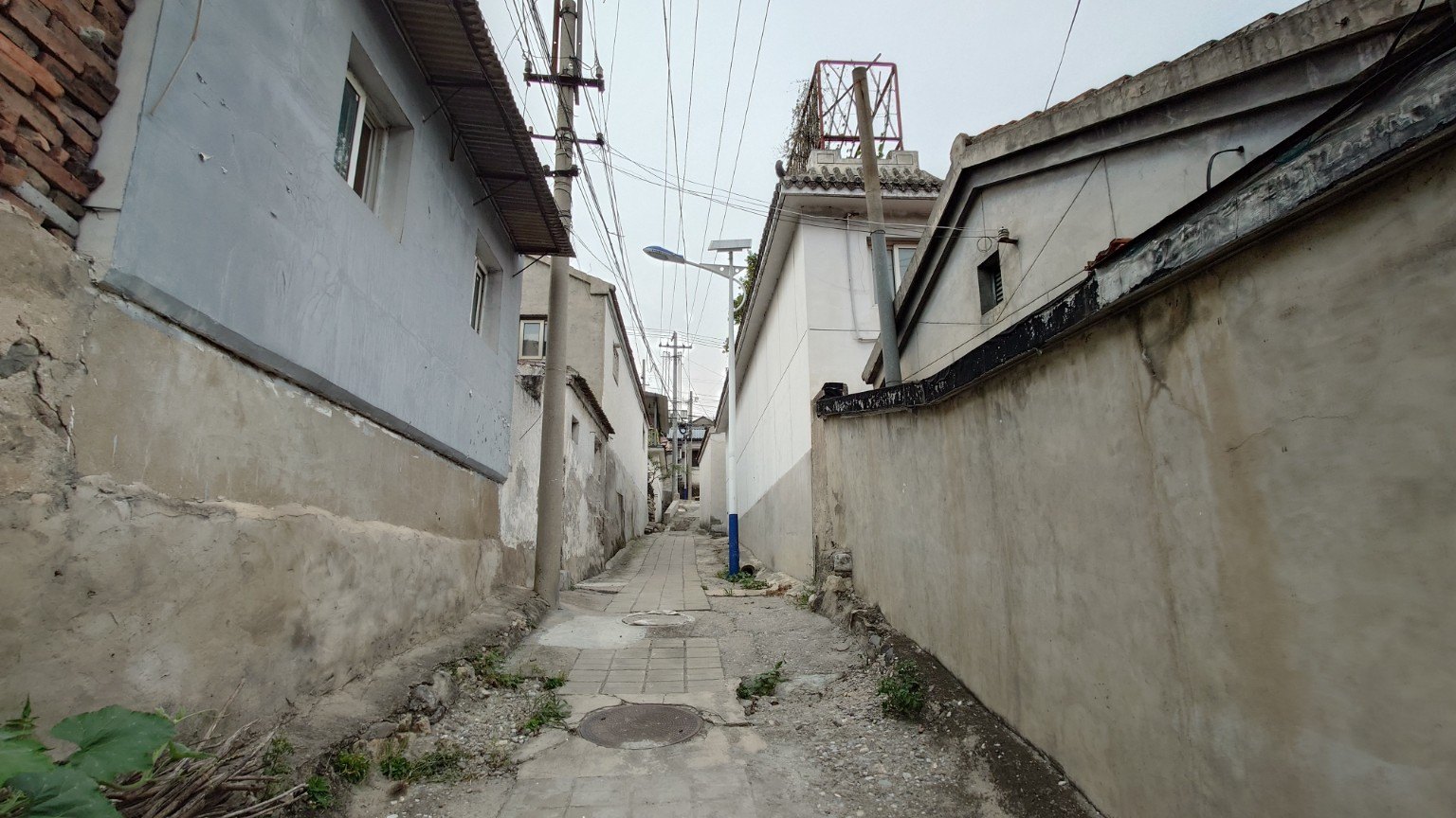 A narrow paved lane between old plastered houses in Yanchi Town, with overhead wires and a solar streetlight