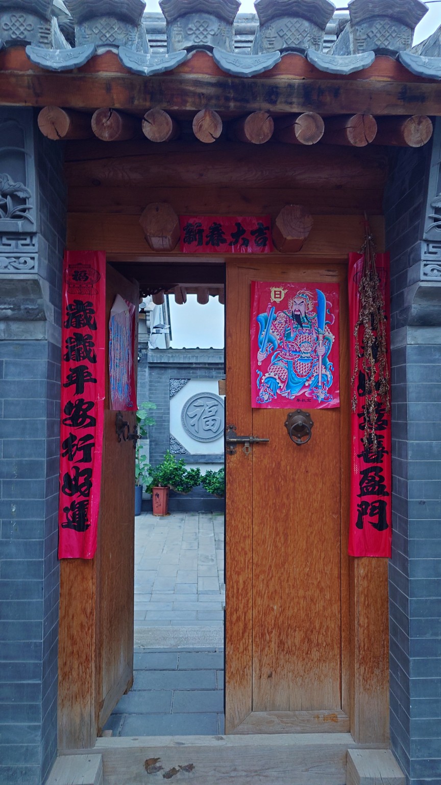 An open timber courtyard gate decorated with Spring Festival couplets and a door-god print