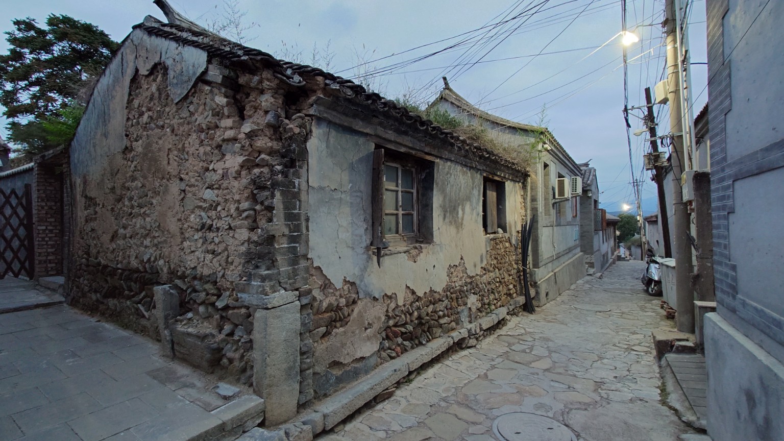 A narrow stone lane passes a weathered traditional house in Lingshui Village, with repaired courtyards continuing downhill