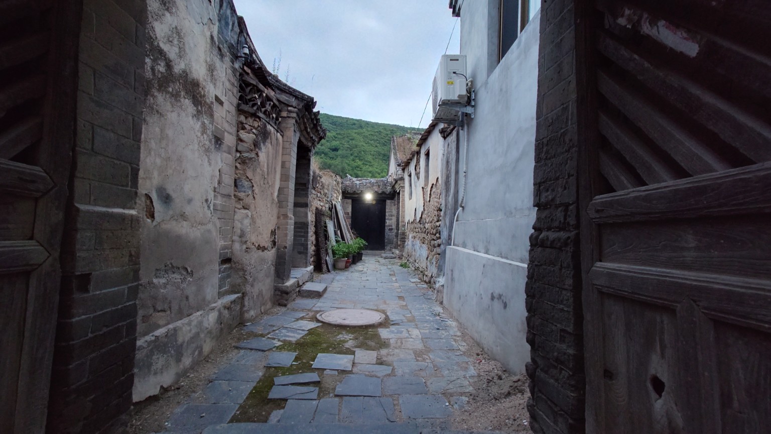 A narrow paved alley between old courtyard walls and repaired village houses in Lingshui