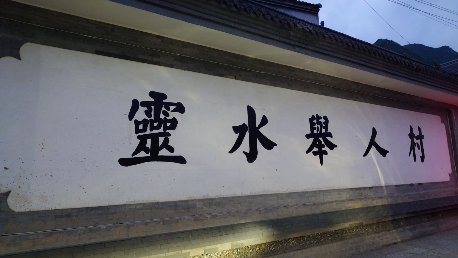 A white village wall bearing the black calligraphy Lingshui Juren Village