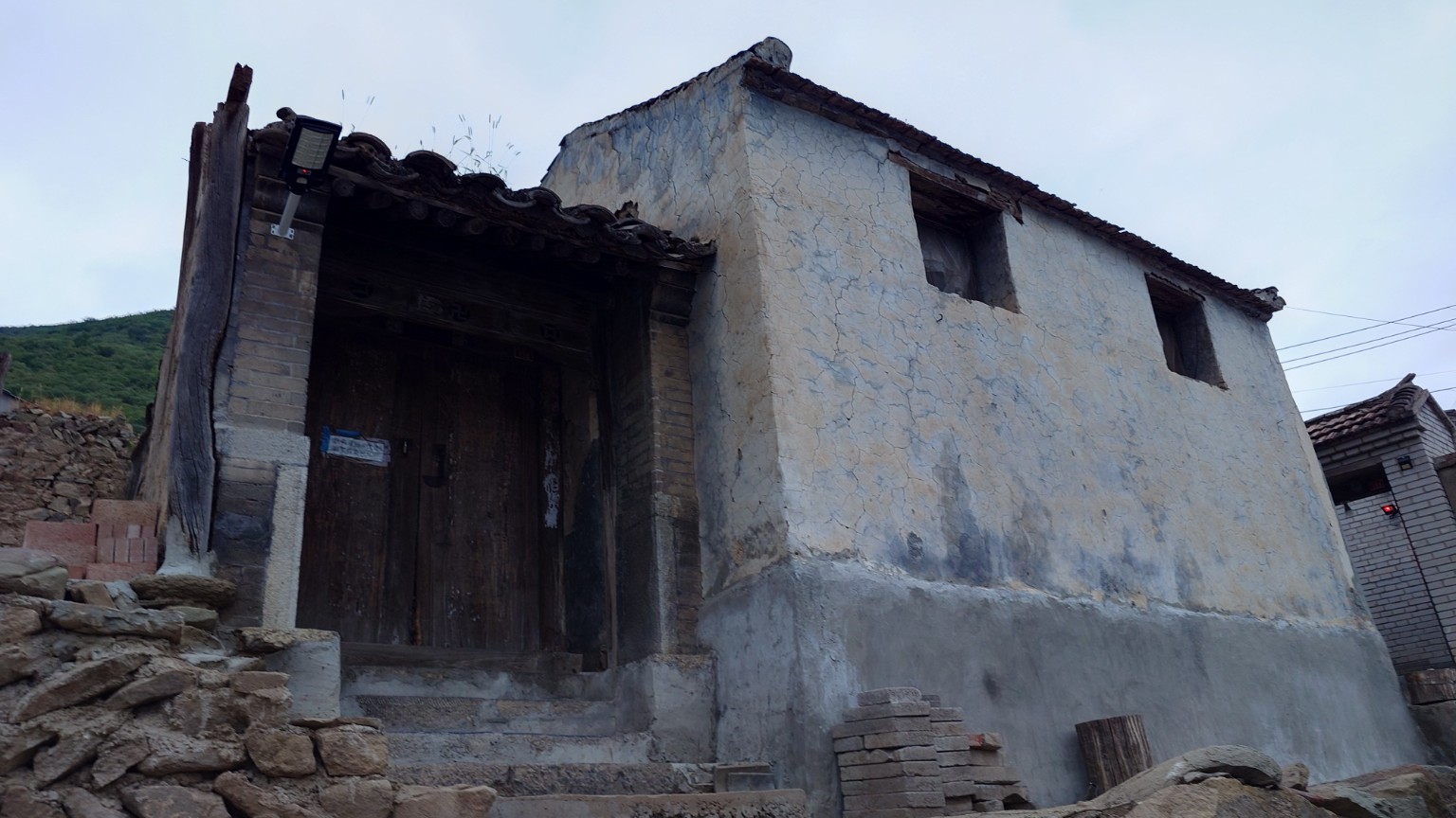 A large traditional house with weathered plaster, timber doors and visible repair materials