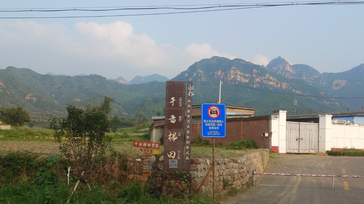 A sign for the Thousand-Mu Terraces scenic area beneath a dramatic mountain ridge
